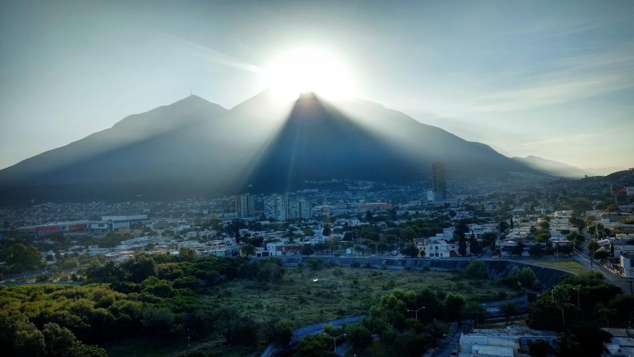 Paisaje urbano al amanecer con montañas al fondo, mostrando un entorno natural.