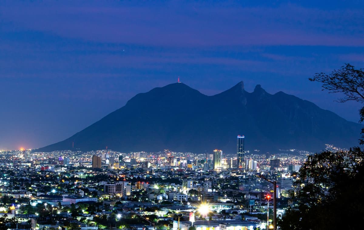 Vista nocturna de una ciudad iluminada con montañas en el fondo, mostrando un paisaje urbano vibrante bajo un cielo azul oscuro, destacando la infraestructura moderna que utiliza tuberías de acero de alta calidad.