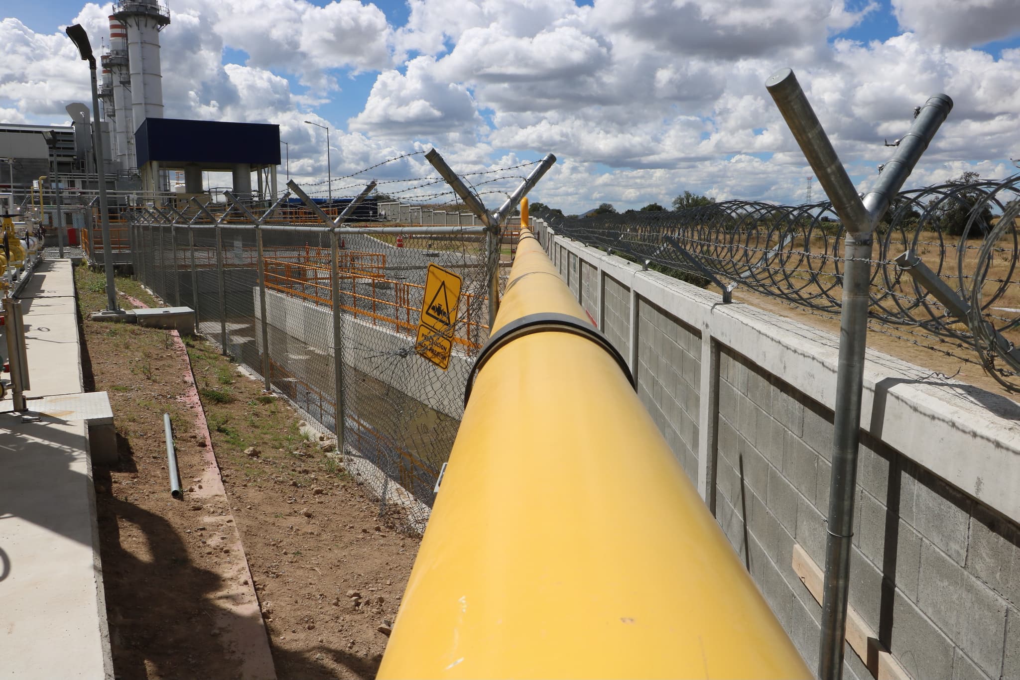 Tubería de acero de gran diámetro colocada a lo largo de un terreno industrial con cercado de seguridad.