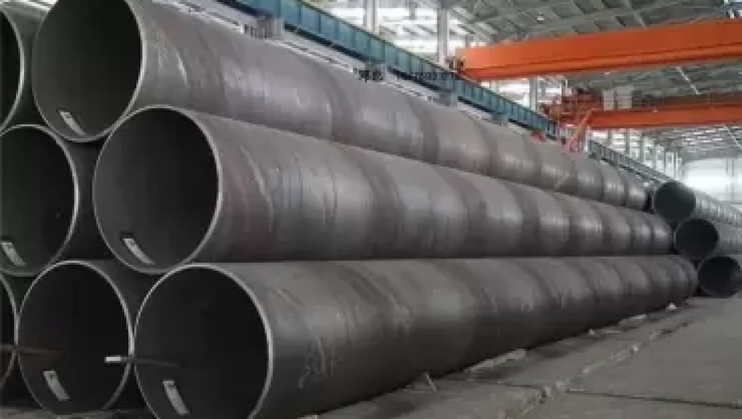 Grandes tuberías de acero apiladas dentro de una fábrica con grúa, subrayando el enfoque de MMTubería en la producción a gran escala y la logística de distribución nacional.