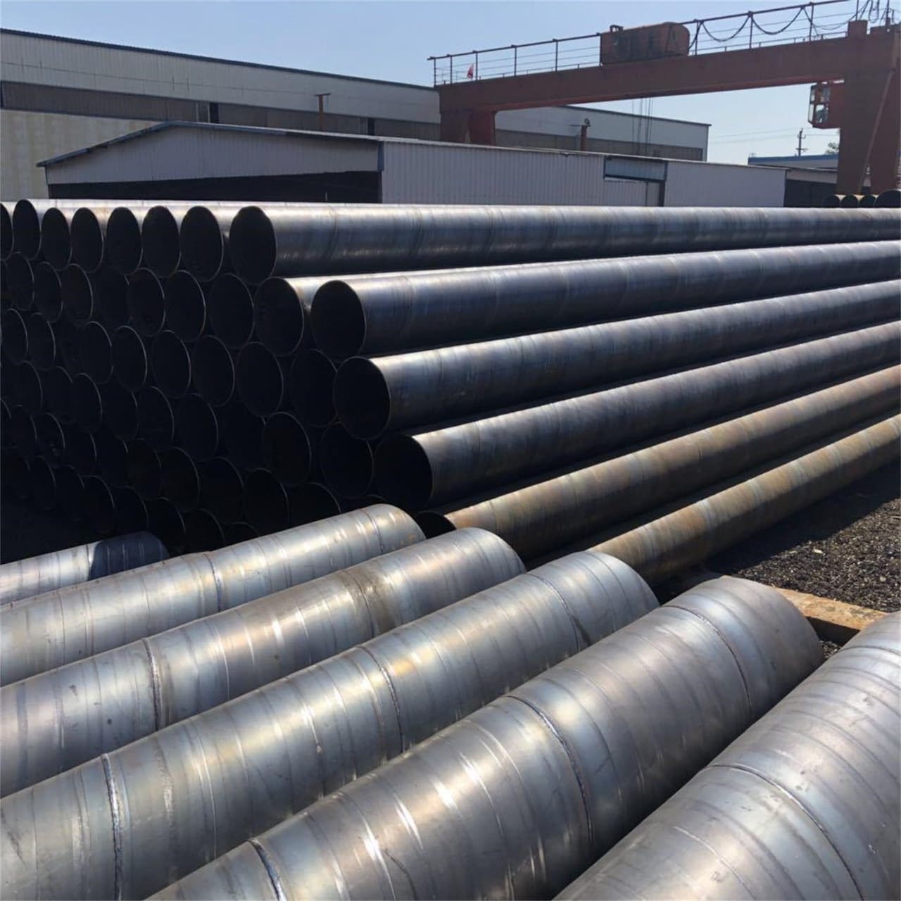 Pilas de tuberías de acero alineadas en el exterior de un almacén, resaltando la disponibilidad y organización logística de MMTubería para proyectos nacionales.