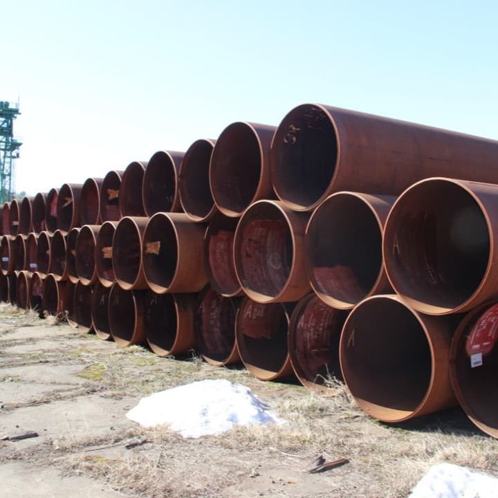 Tuberías de acero apiladas en una instalación industrial, destacando su robustez y acabado mate. El proceso de fabricación asegura alta calidad y durabilidad
