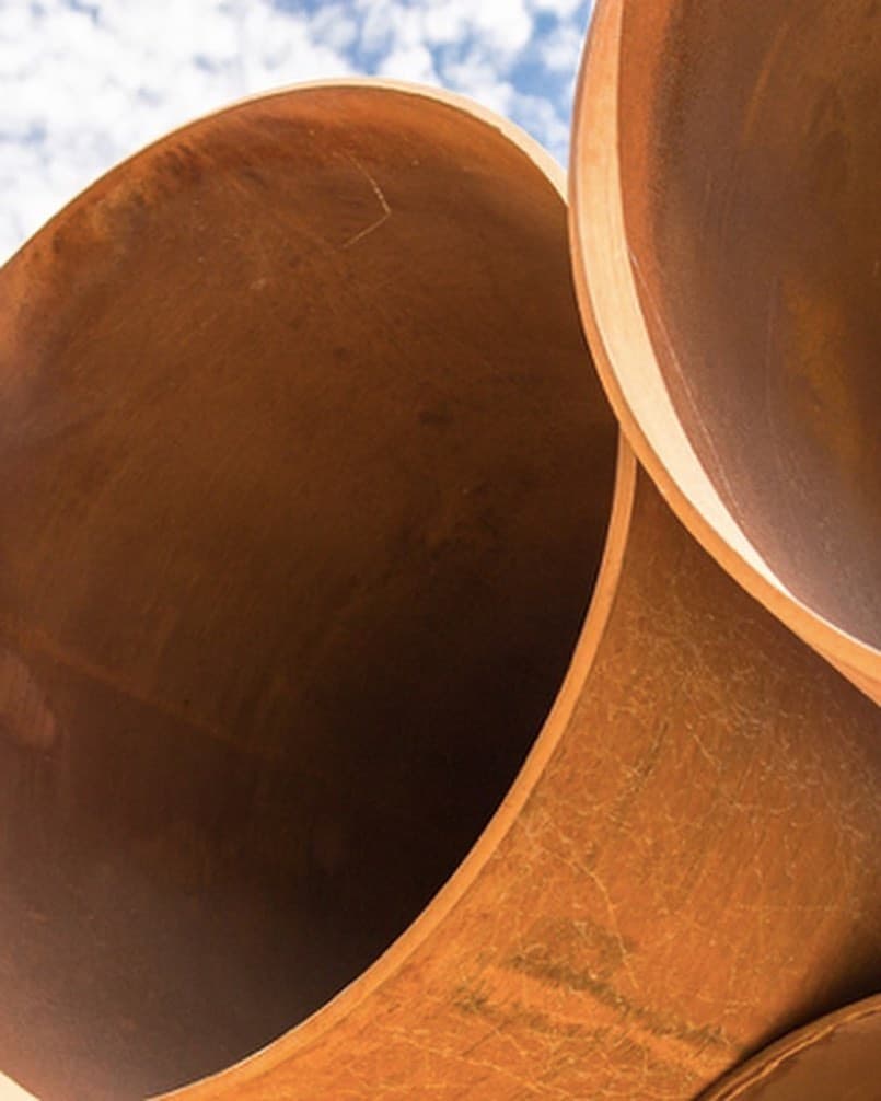 Pilas de tuberías de acero de gran diámetro en una planta industrial, listas para distribución, destacando la alta calidad y el alcance nacional de MMTubería.