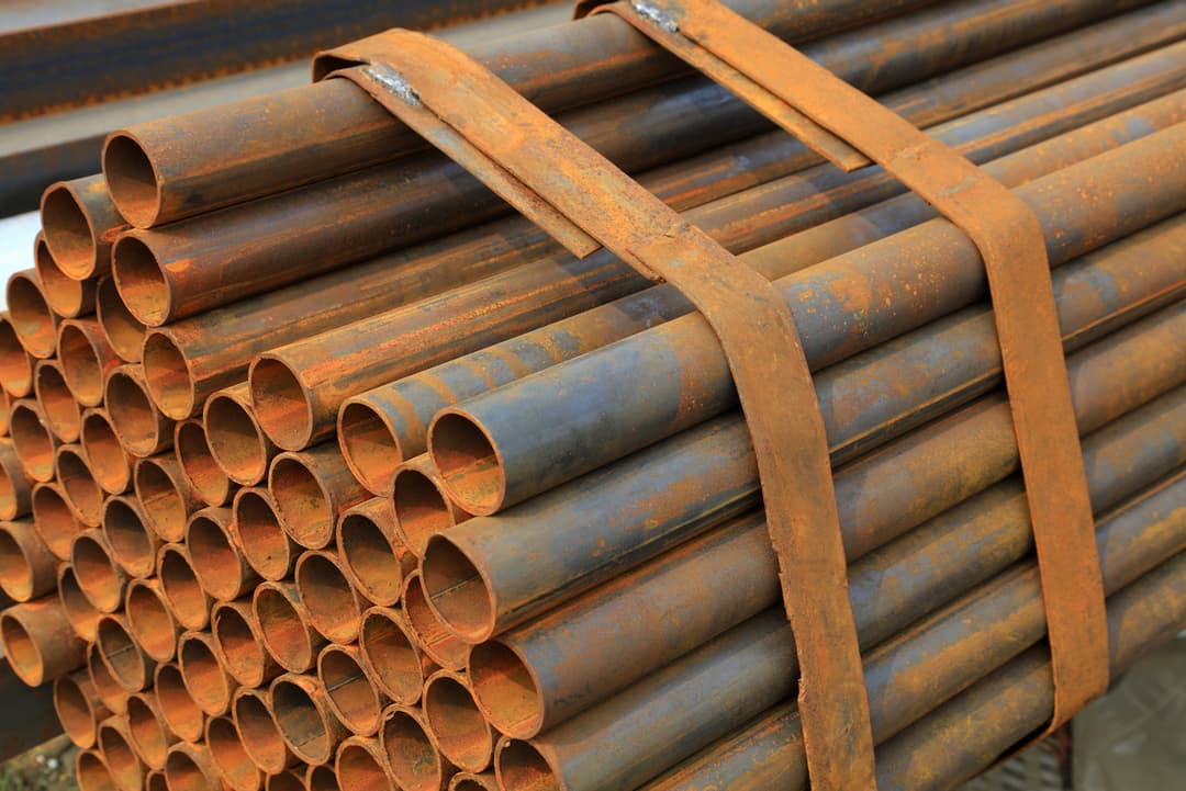 Pilas de tuberías de acero oxidadas, almacenadas en el exterior, demostrando la durabilidad y la resistencia de los materiales a pesar de la exposición a elementos exteriores.