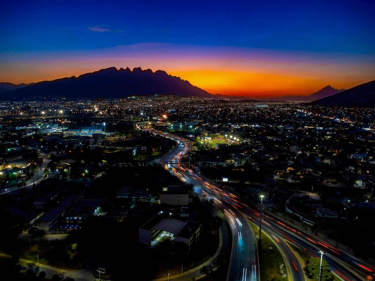 Vista nocturna de una ciudad con carreteras iluminadas y una montaña al fondo, representando el alcance nacional de MMTubería en la infraestructura vial y urbana de México.